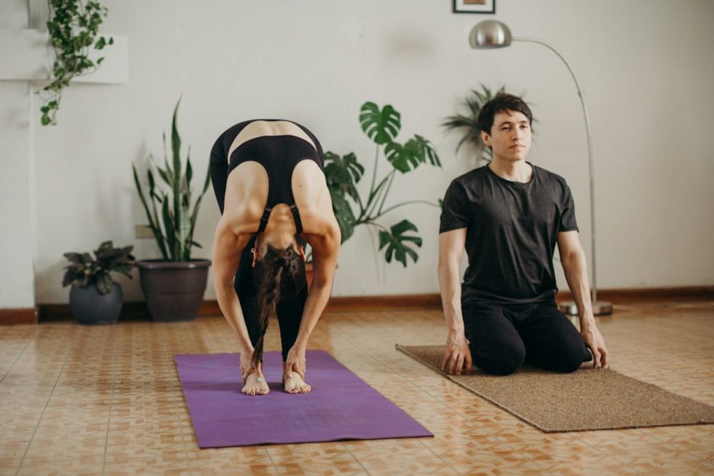 Un homme et une femme s'entraînent sur un tapis de yoga, lors d'un cours dans une salle épurée.