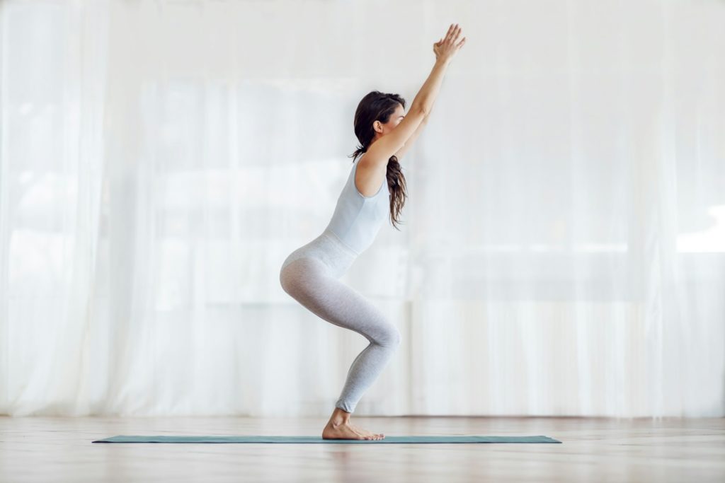 Une sportive vêtue de blanc fait une posture de yoga dans une salle lumineuse.