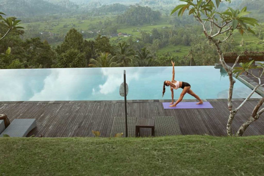 Une pratiquante de yoga effectue une posture du triangle près d'une piscine.