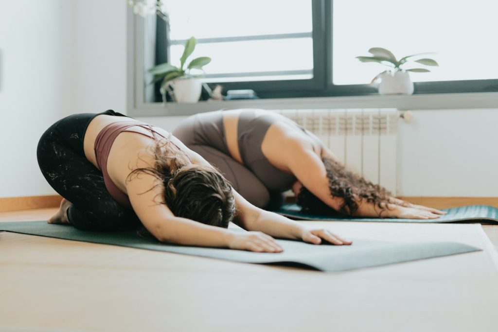 Deux pratiquantes de yoga font une posture d'assouplissement au sol sur un tapis.