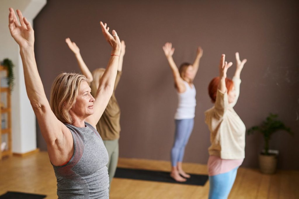 Des élèves lors d'une séance de yoga font un posture avec les mains en l'air.