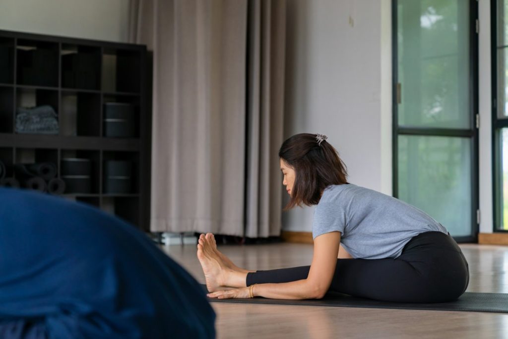 Une femme asiatique vue de profil en train de faire une posture de la pince assise.