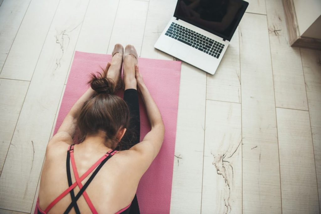 Une femme photographiée de haut dans une pose de yoga devant son écran.