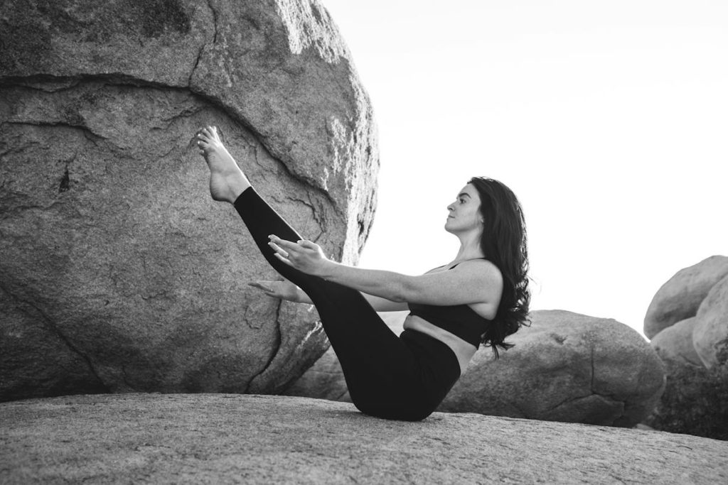 Une pratiquante de yoga fait une posture de yoga plutôt complexe sur des rochers.