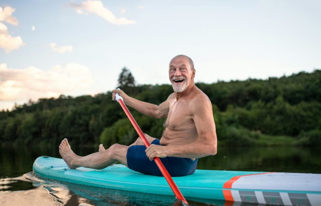 Un vieux sourit sur son canoë en ramant les jambes tendues.