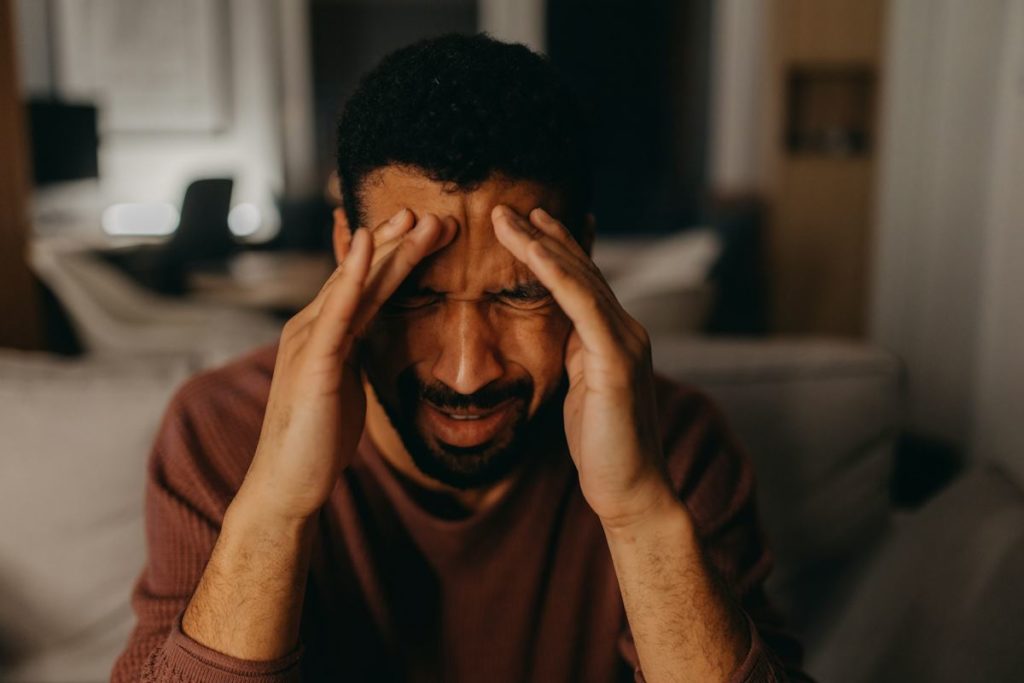 Un homme se tient la tête et semble avoir beaucoup de douleurs.