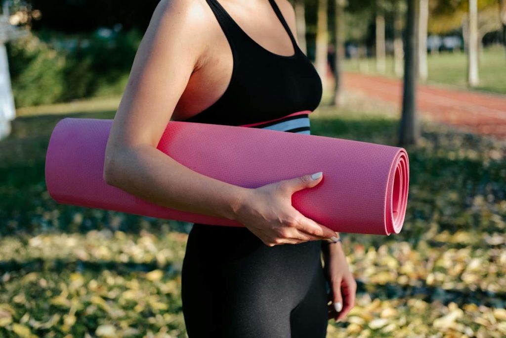 Vue de profil d'une femme qui porte un tapis en tenue de sport.