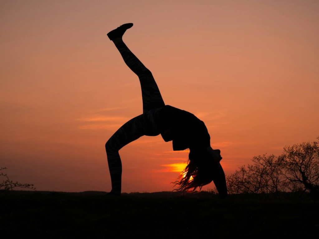 Une fille vue de côté en train de faire la roue au coucher du soleil.