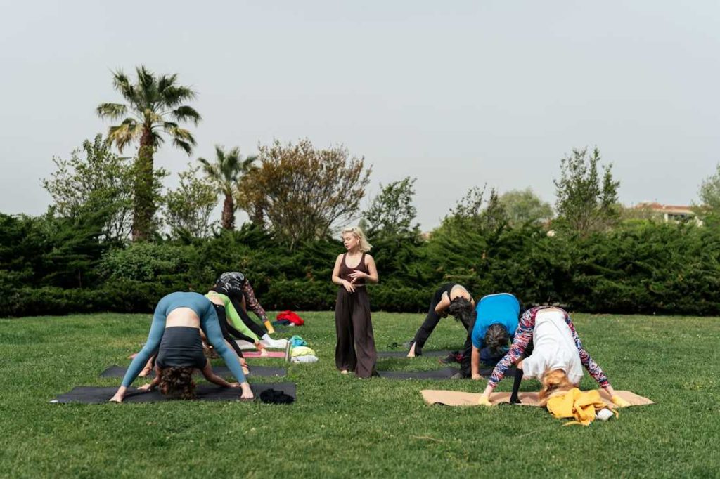 Un groupe de personnes font une posture de yoga avec la tête vers le bas, dans l'herbe.