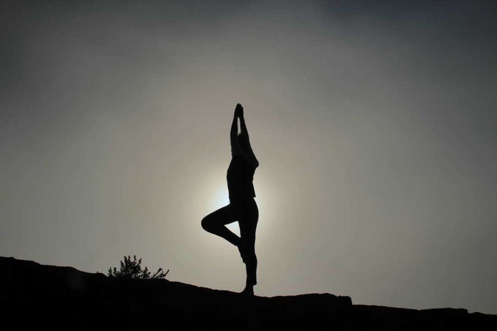 Une personne fait du yoga lors du coucher de soleil dans une atmosphère sombre.