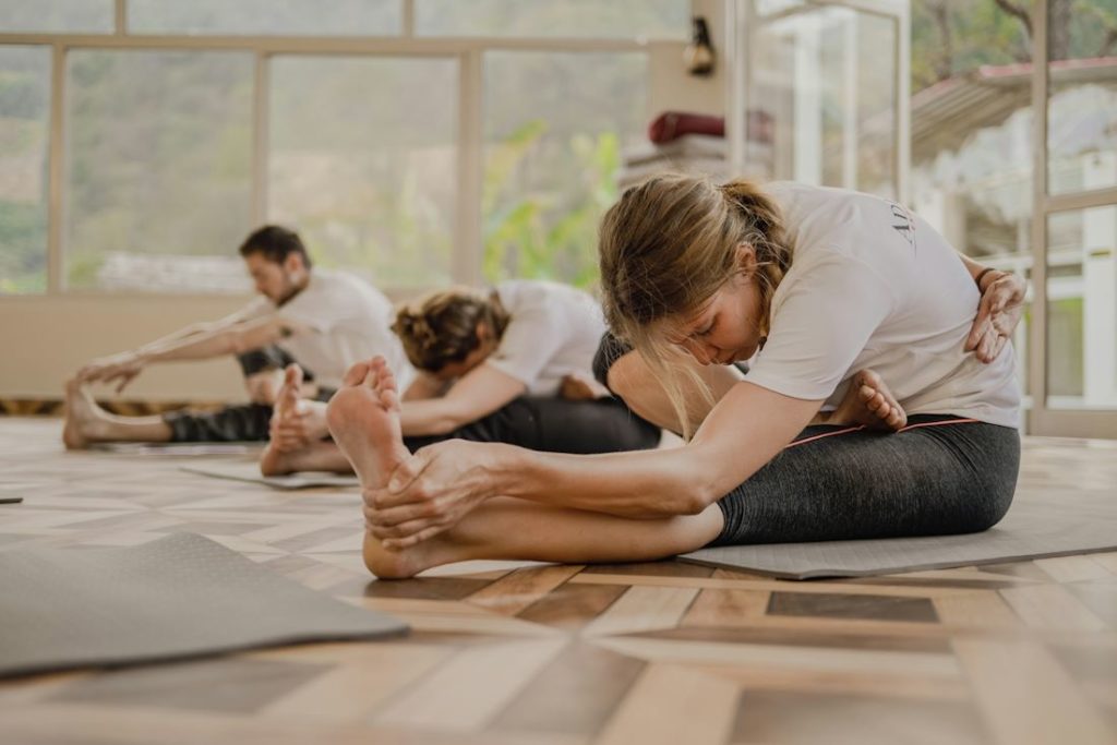 Des pratiquants d'une salle de yoga font des étirements assis, au sol.