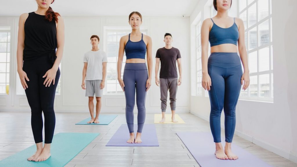 Une séance de yoga avec des pratiquants debout, dans une pièce lumineuse, éclairée en blanc.