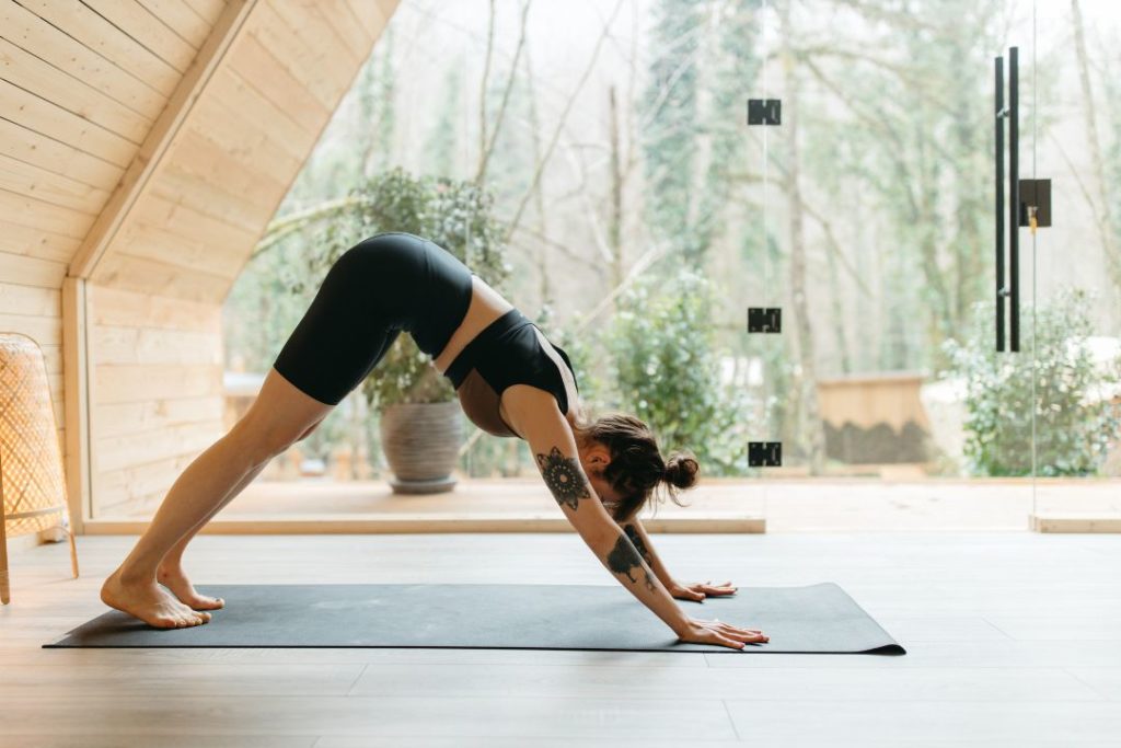 Une sportive en tenue de sport fait une posture de yoga célèbre sur un tapis noir.