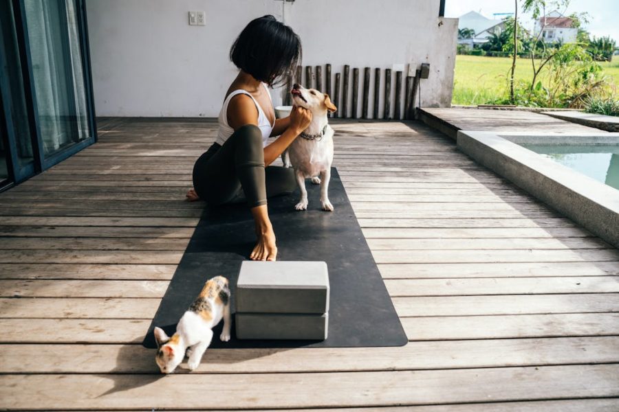 Une femme sur un tapis de yoga, caresse un chien et a un chat au niveau des pieds.