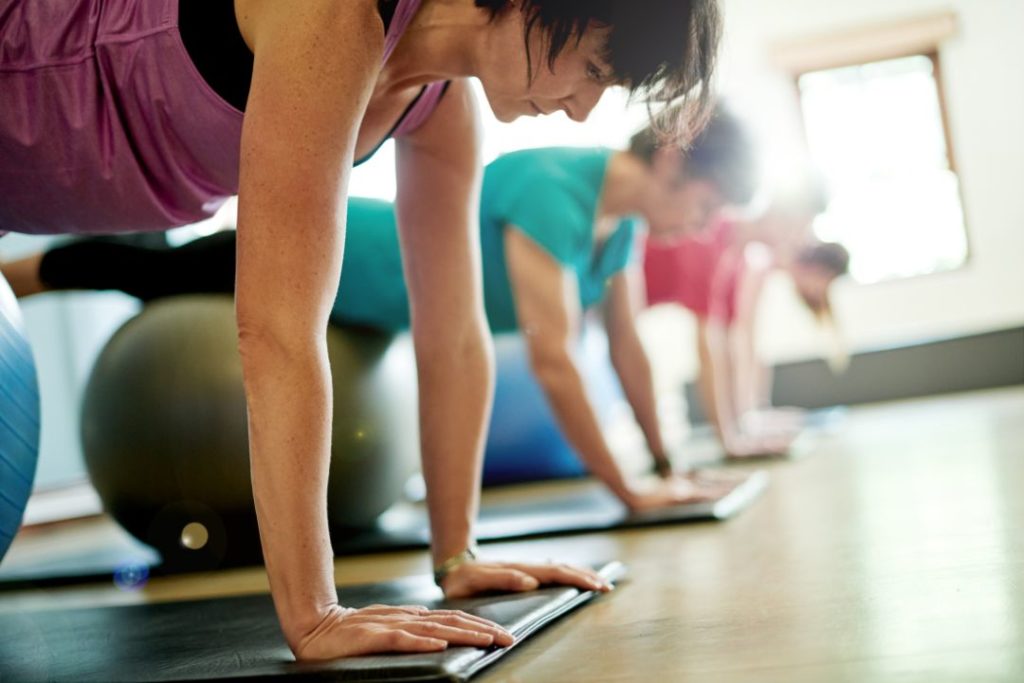 Des pratiquants d'une salle de sport font des exercices de gainage avec un ballon gonflable.