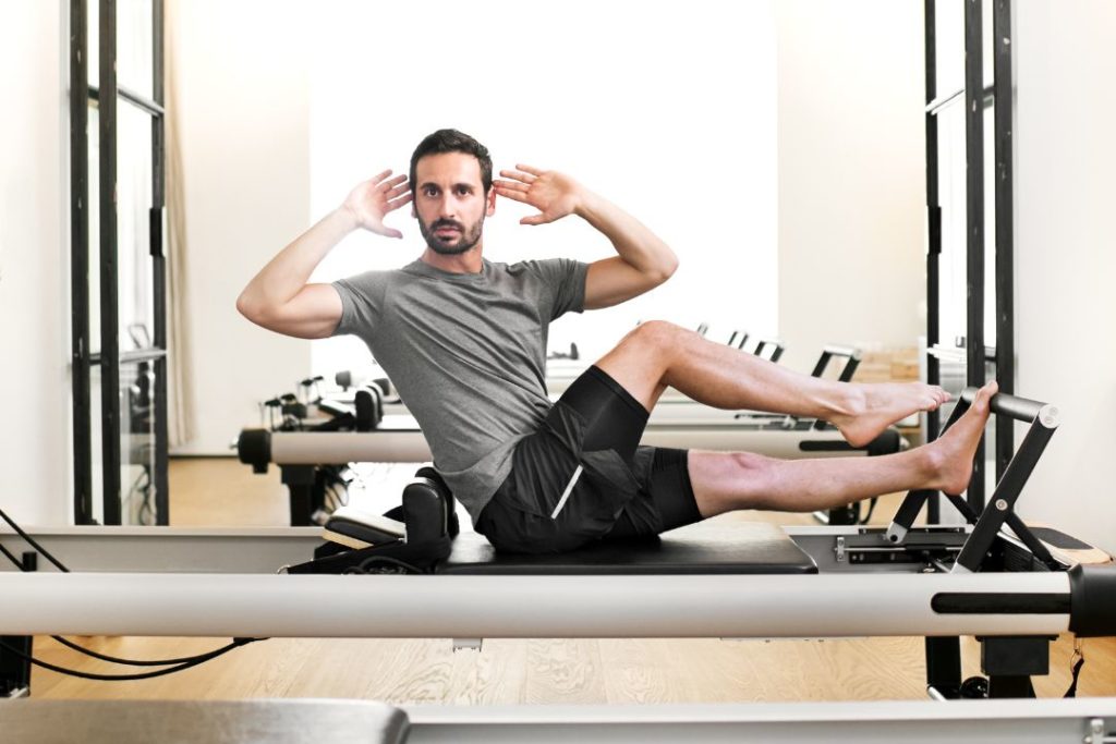 Un homme travaille ses abdominaux sur une machine Reformer de Pilates.