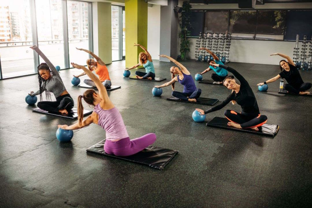 Un groupe de personnes font des postures et des exercices dans un studio de Pilates.