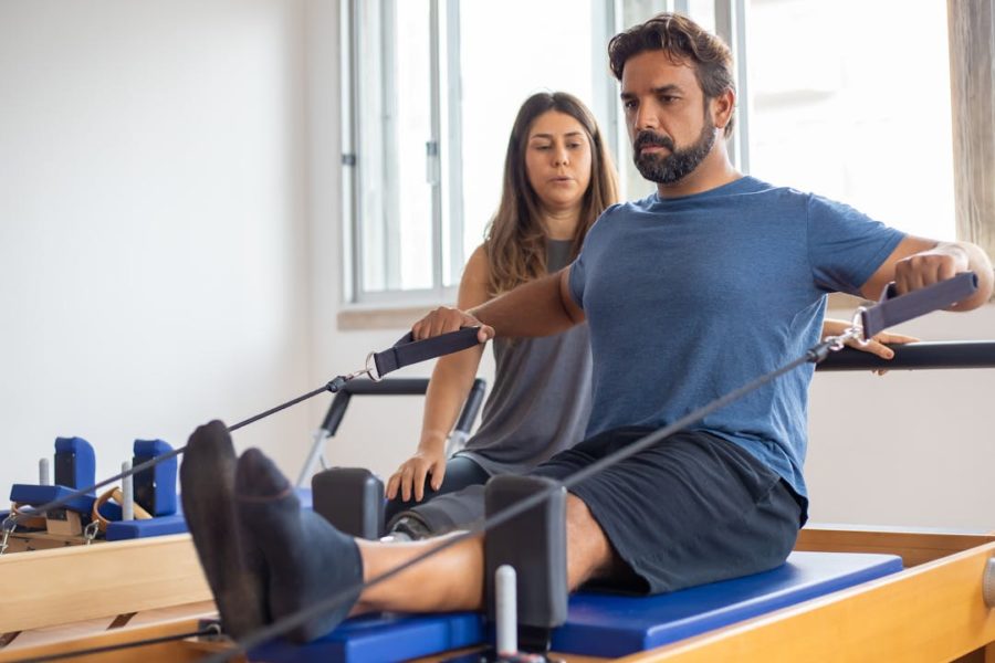 Un homme fait du rameur en étant supervisé par une coach sportif.