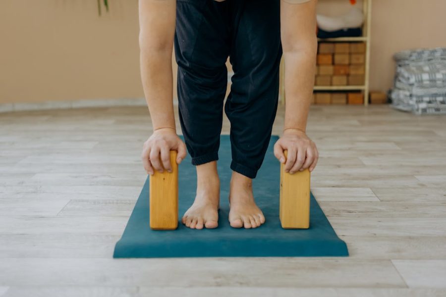 Une femme tient à bout de bras des briques de yoga posées debout sur le tapis de gym.